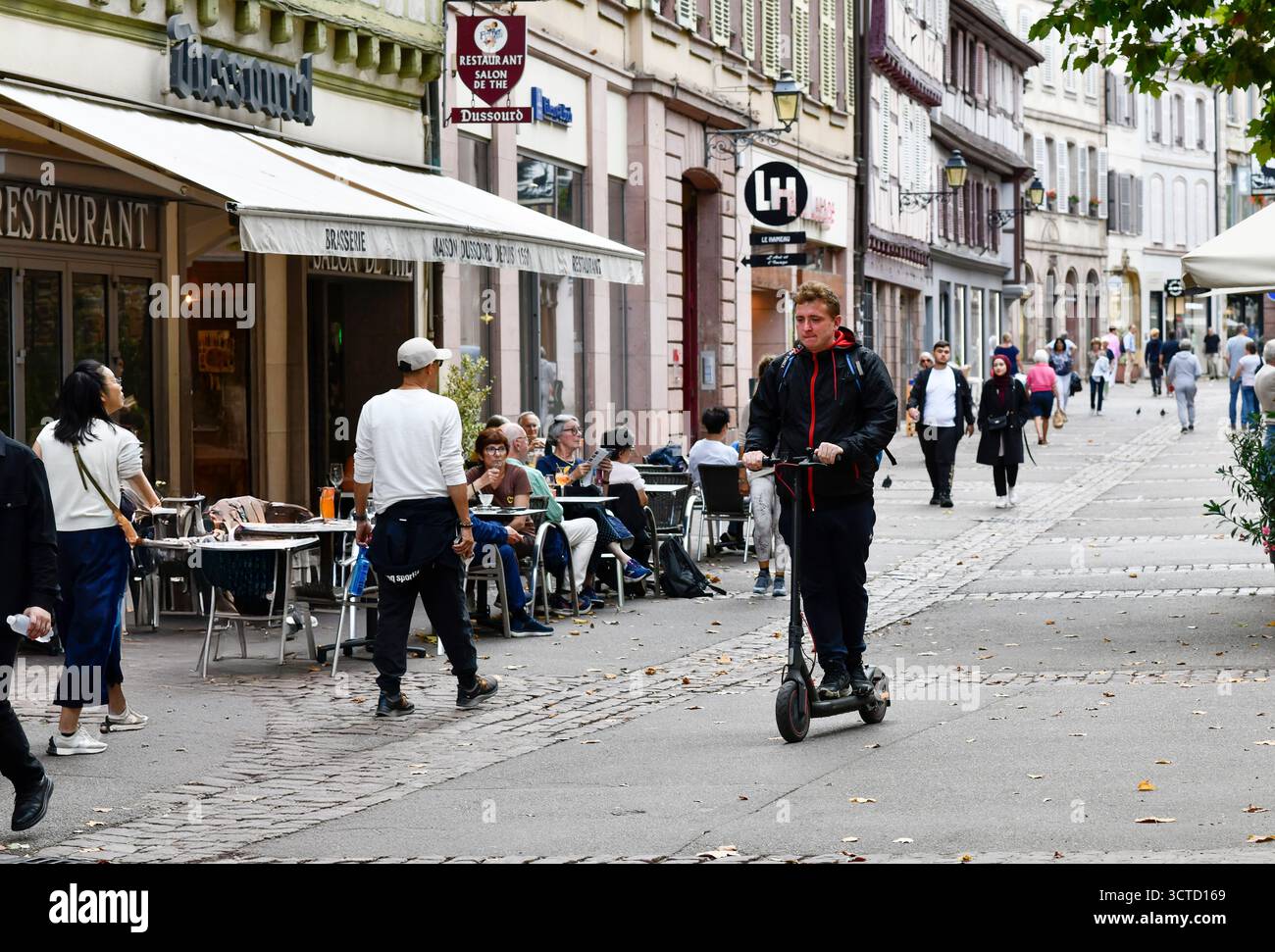 Junger Mann, der auf einer Straße in Colmar im Elsass in Frankreich mit Elektroroller fährt. Stockfoto