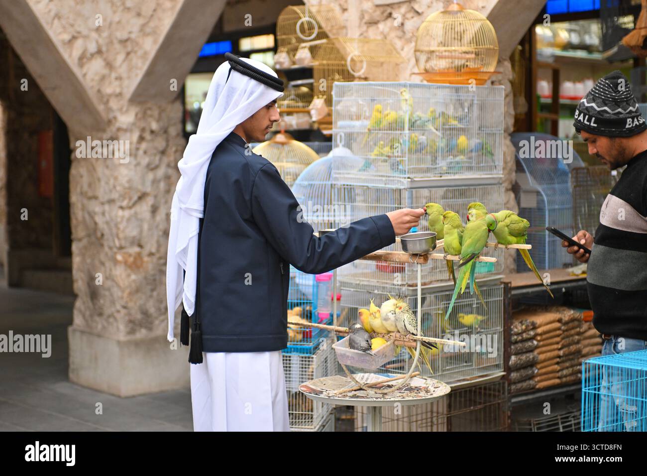 Katar, Doha: Vogelmarkt am Souk Waqif. Verkäufer traditioneller Kleidung mit Keffiyeh, Sittichen, Käfigen und Papageien Stockfoto