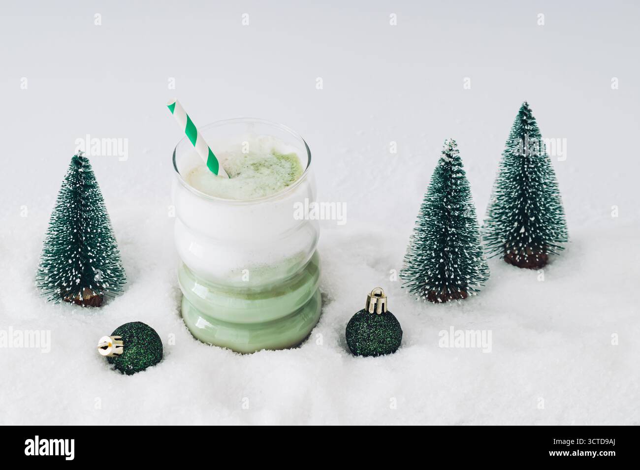 Weihnachtskomposition mit Matcha Latte und Weihnachtsbäumen und Dekorationen auf schneebedecktem Hintergrund. Minimales Weihnachts- und Neujahrskonzept. Stockfoto