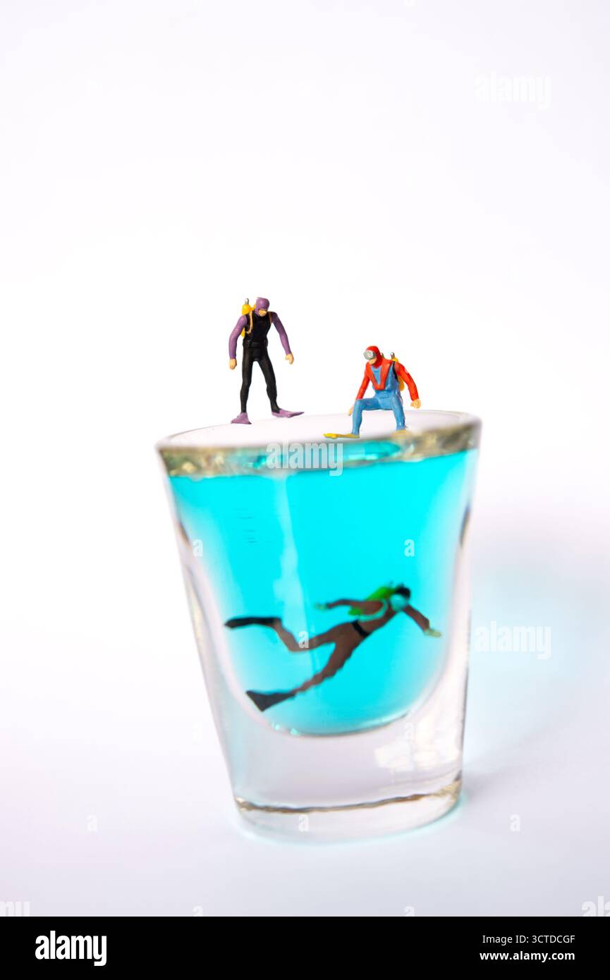 Miniaturtaucher erkundet das Blaue Wasser in einem Glas, während kleine Beobachter von oben zusehen – Creative Conceptual Photography Scene Stockfoto
