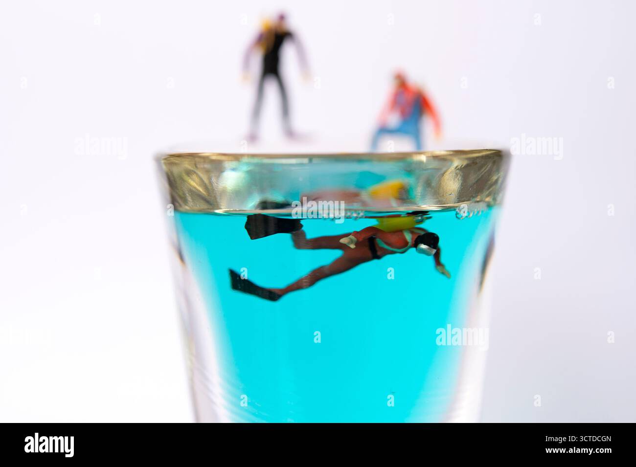Winzige Taucher bereiten sich auf das Abenteuer vor, stehen am Rand des Glases gefüllt mit blauer Flüssigkeit – Creative Miniatur Photography Concept Stockfoto