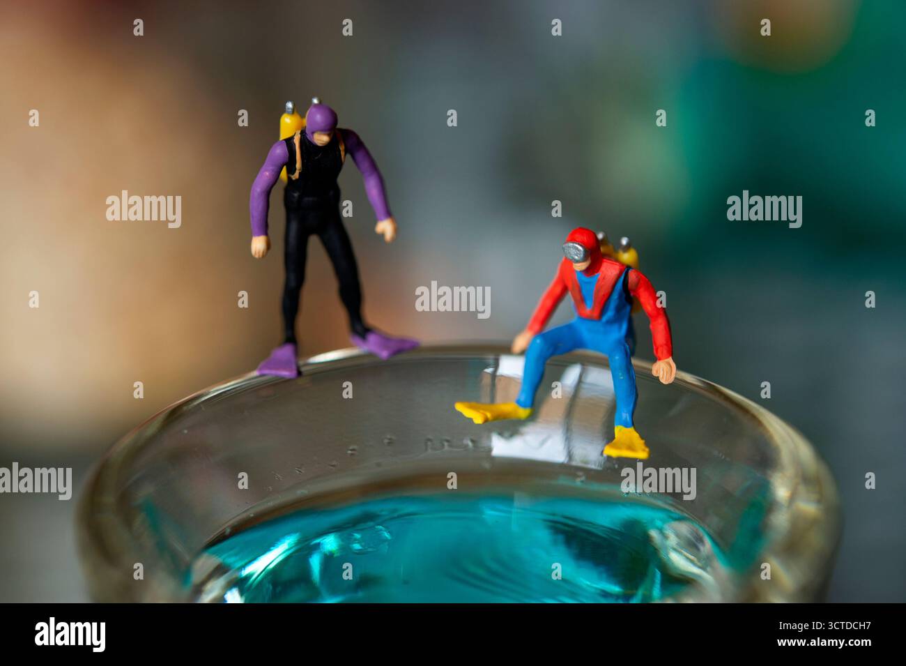Winzige Taucher bereiten sich auf das Abenteuer vor, stehen am Rand des Glases gefüllt mit blauer Flüssigkeit – Creative Miniatur Photography Concept Stockfoto
