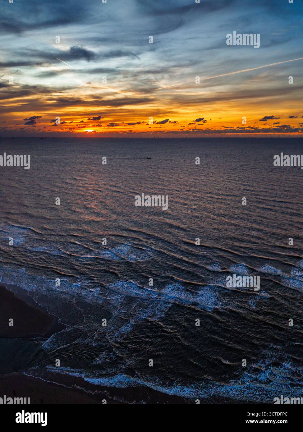 Aus der Vogelperspektive auf den Sonnenuntergang an der Küste mit goldenem Licht, das auf sanften Wellen reflektiert, Schaum und entferntes Schiff verleihen dem ruhigen Ozeanhorizont ben Tiefe Stockfoto