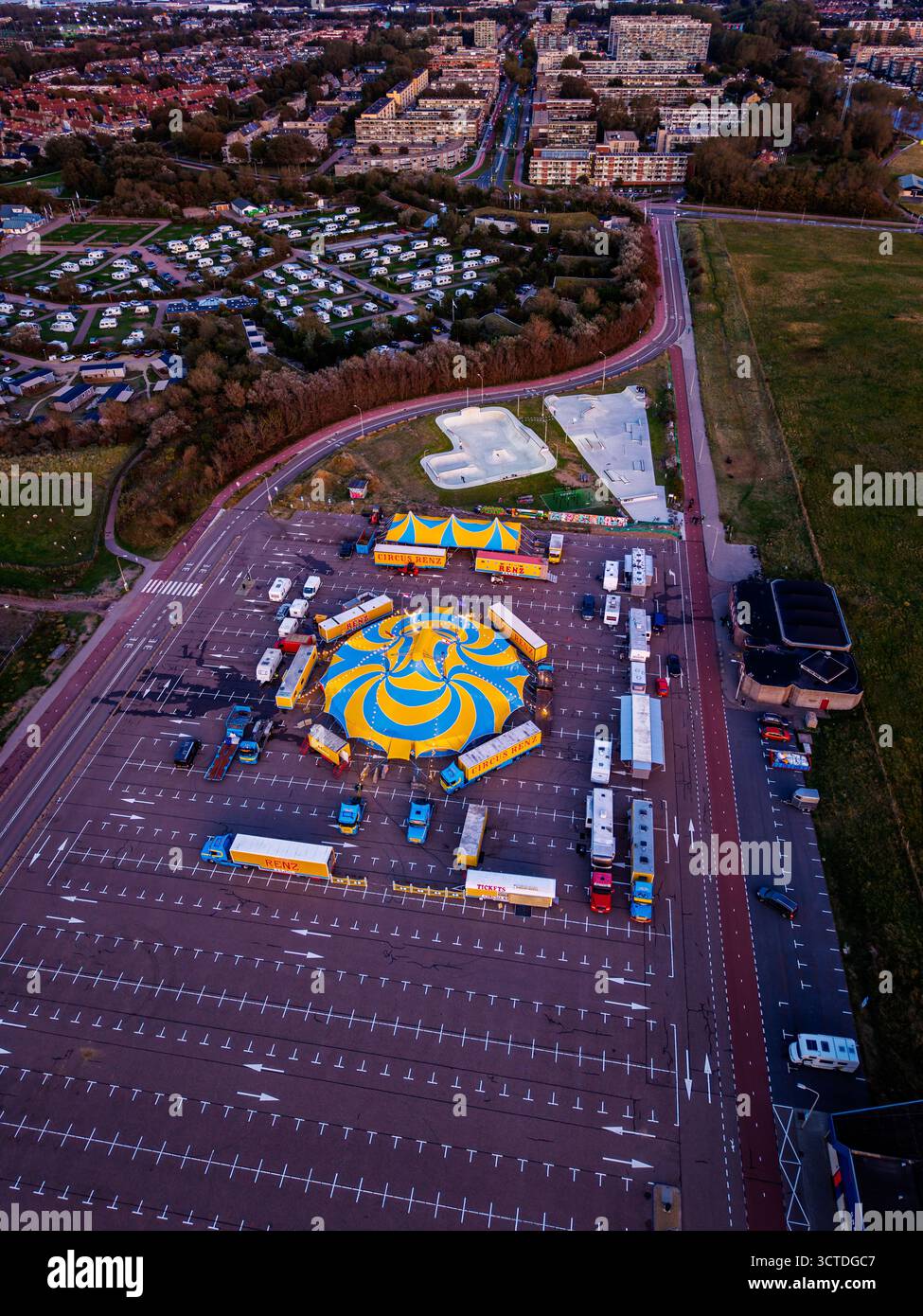 Aus der Vogelperspektive des Zirkus auf dem Parkplatz neben dem Skatepark und der Wohnzone, gelb-blaues Zelt, Anhänger und Rampen stehen im Kontrast zu gedämpften Stadttönen Stockfoto