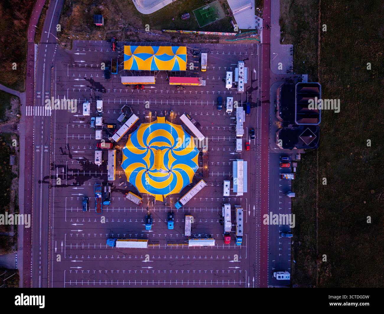 Aus der Vogelperspektive des pulsierenden Zirkus auf dem Parkplatz, blaugelbes Spiralzelt umgeben von Anhängern und kleineren Zelten, zeigt organisierte Logistik und Stockfoto