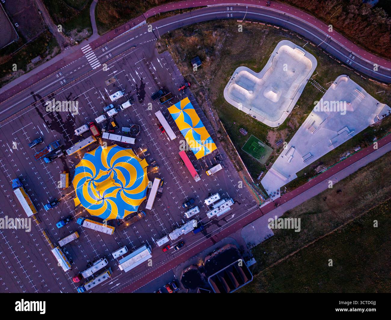 Aus der Vogelperspektive des Zirkus auf dem Parkplatz neben dem Skatepark und der Wohnzone, gelb-blaues Zelt, Anhänger und Rampen stehen im Kontrast zu gedämpften Stadttönen Stockfoto