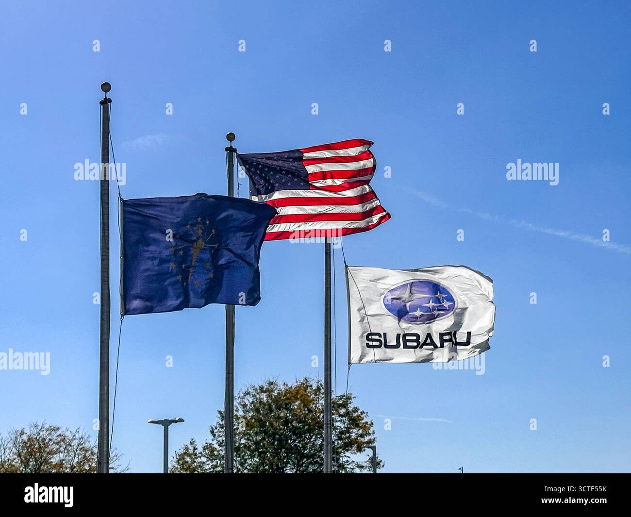 Subaru-Flagge, Indiana-Staatsflagge und eine amerikanische Flagge, die in einem Subaru-Händlerbetrieb gegen den blauen Himmel fliegen - Smartphone-aufgenommenes Stockfoto
