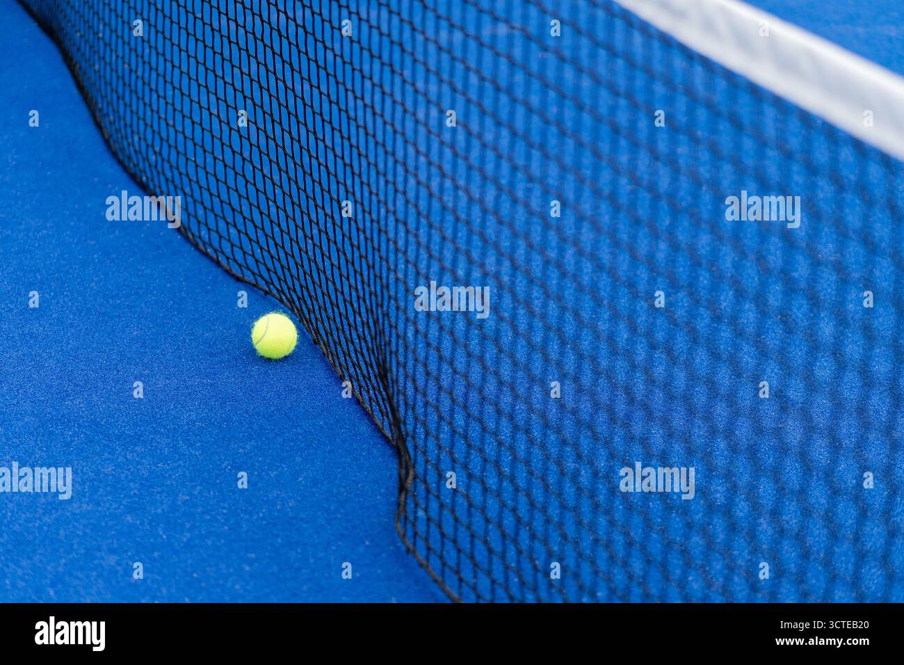 Gelber Ball auf dem Boden hinter dem Paddle oder Tennisnetz auf dem blauen Platz im Freien oder drinnen. Tennis- oder Padel-Platz Stockfoto