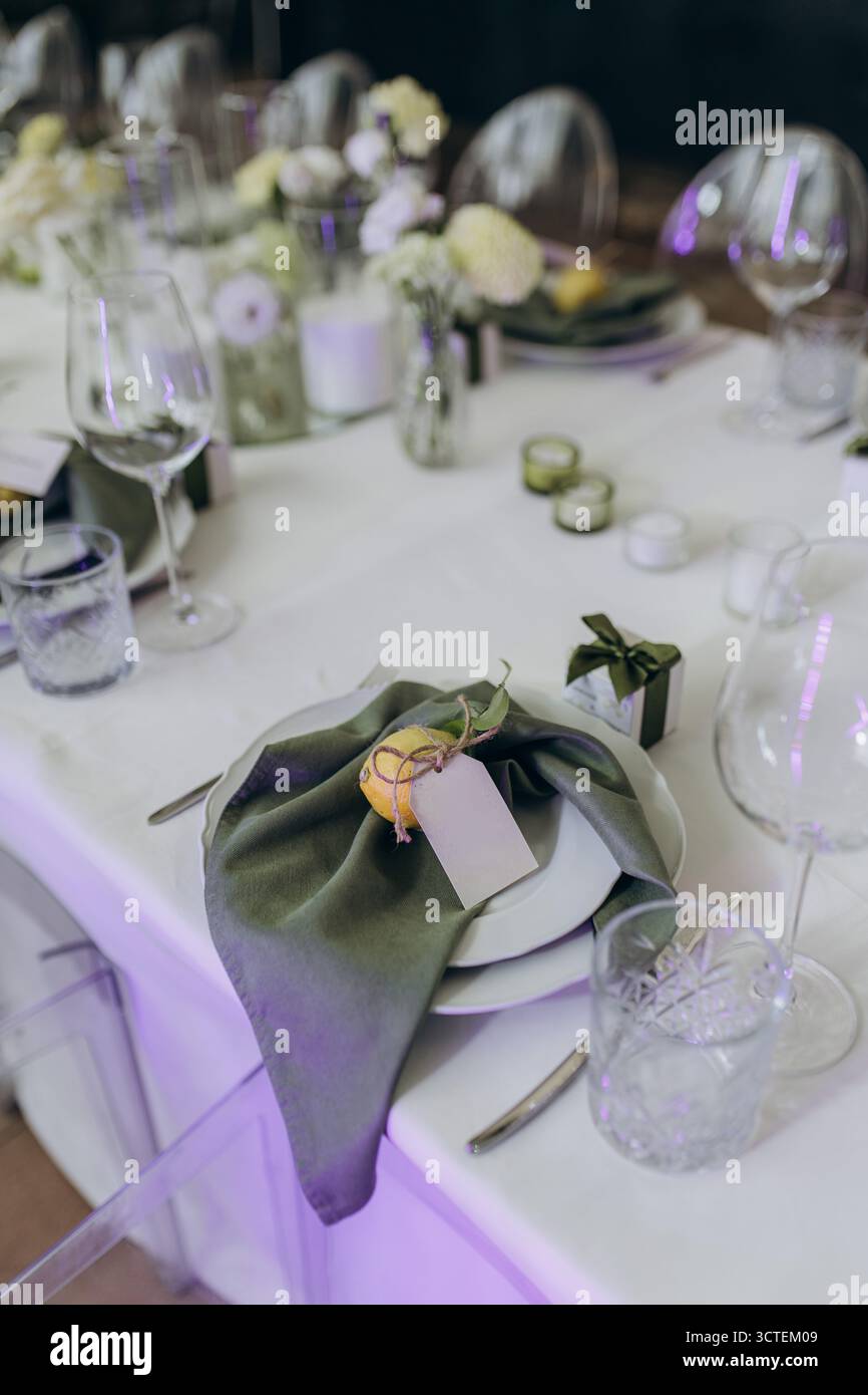 Dieses Bild zeigt eine wunderschön angeordnete Tischdekoration mit einer grünen Serviette und einer dekorativen Zitrone für eine elegante Note, die florale ce-farbe unterstreicht Stockfoto