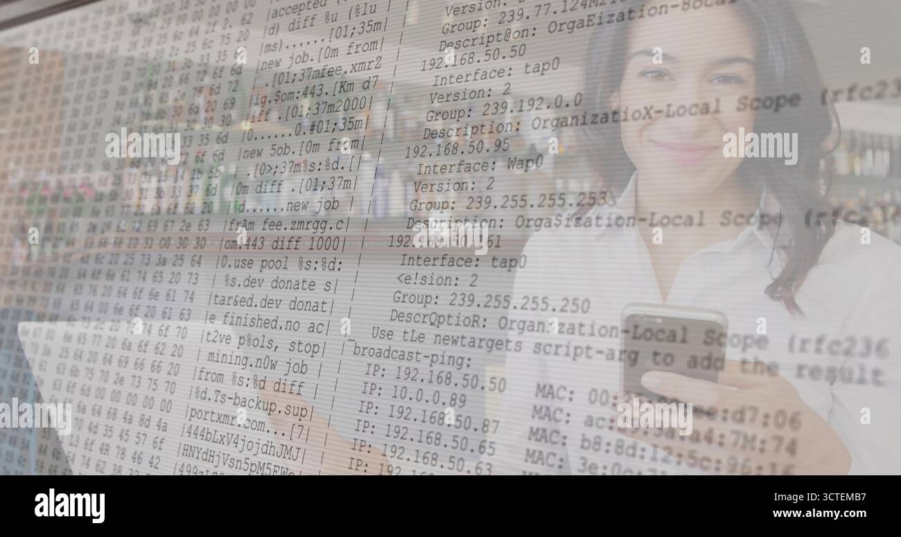 IT-Profi, der das Smartphone hält und am Schreibtisch auf einem Laptop schreibt, mit Code-Overlay Stockfoto