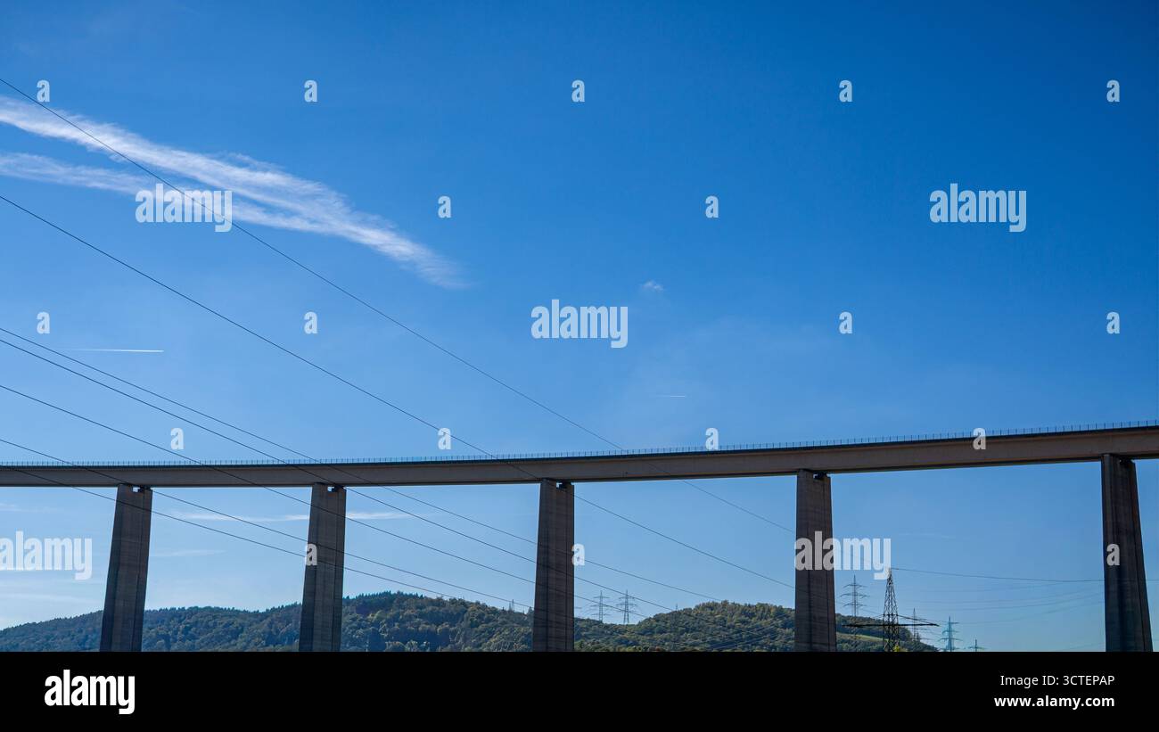 Minimalistischer Blick auf eine hohe Betonbrücke mit Stromleitungen vor klarem blauem Himmel, die moderne Technik und Infrastruktur symbolisiert. Stockfoto