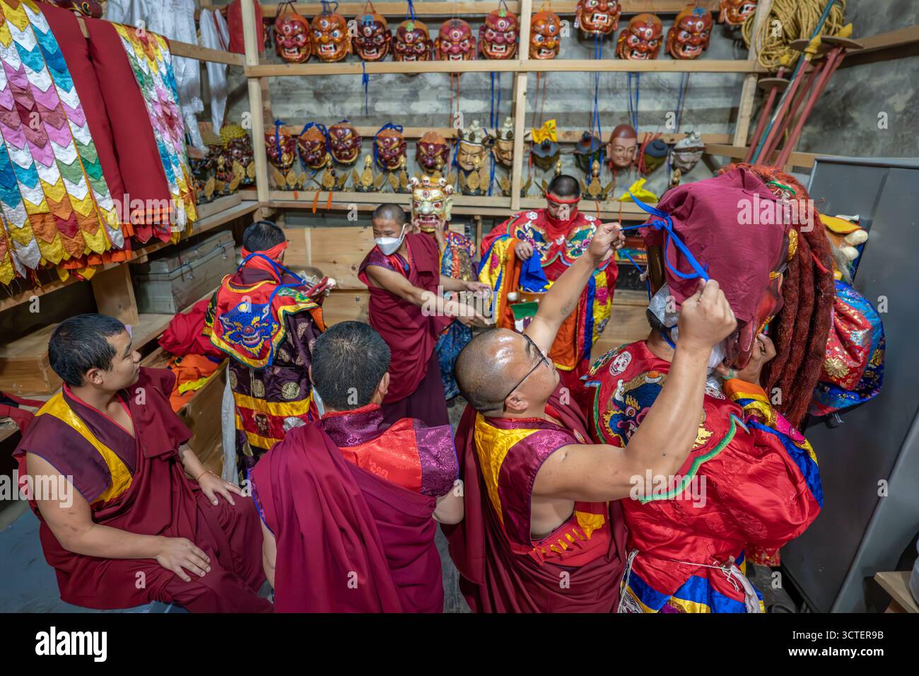 [Jakar], [Bhutan] - 24. September 2025: Blick auf Mönche, die sich auf ein heiliges Tanzritual vorbereiten, inmitten lebendiger Kostüme und kunstvoller Masken, die lange Schatten im schwach beleuchteten Raum werfen. Stockfoto