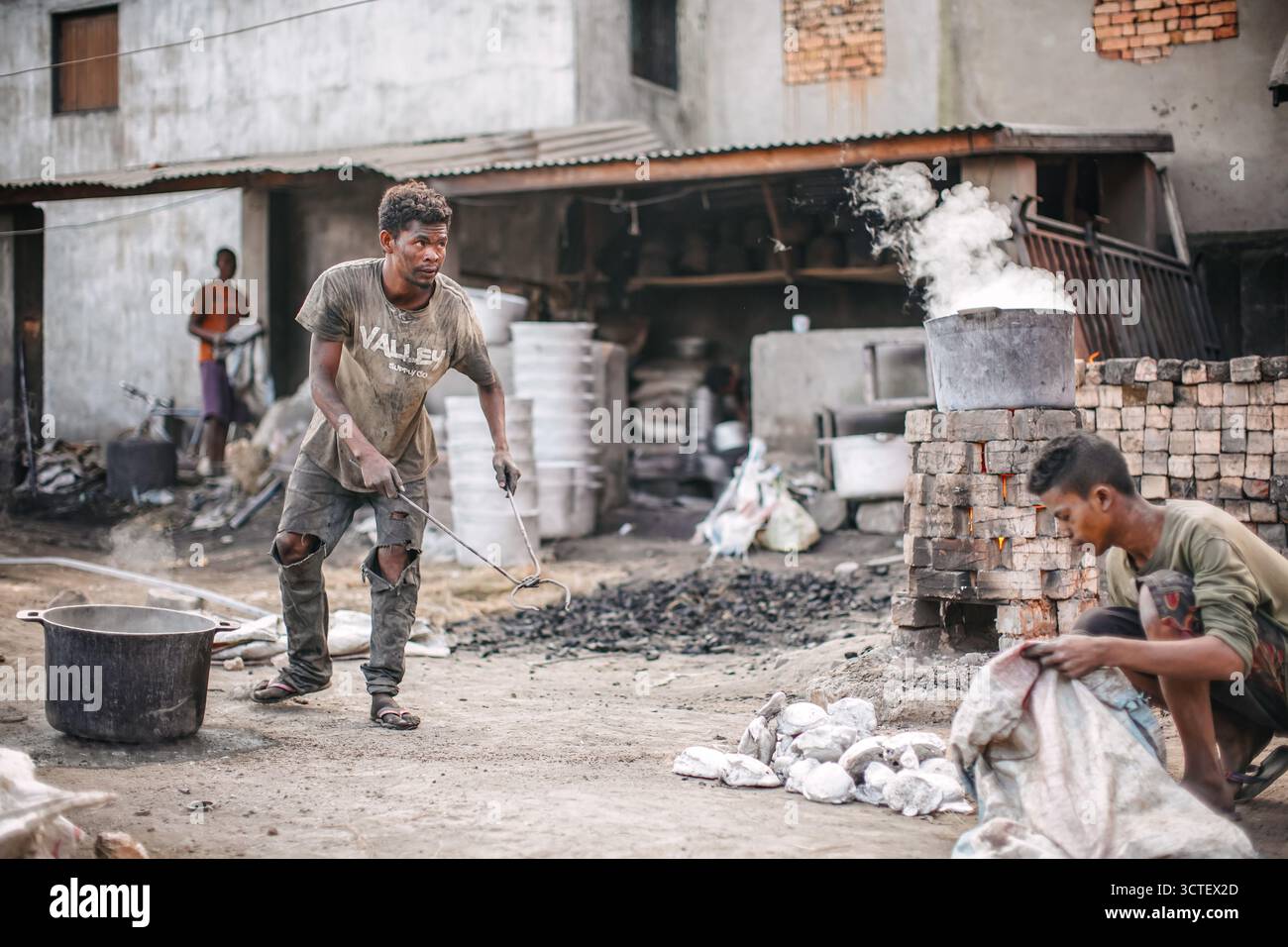 Ambatolampy, Madagaskar - 25. April 2019: Aluminiumverarbeitungsfabrik, Dosen schmelzen in Töpfen über Feuer draußen, Dampf oben, unbekannter Arbeiter h Stockfoto