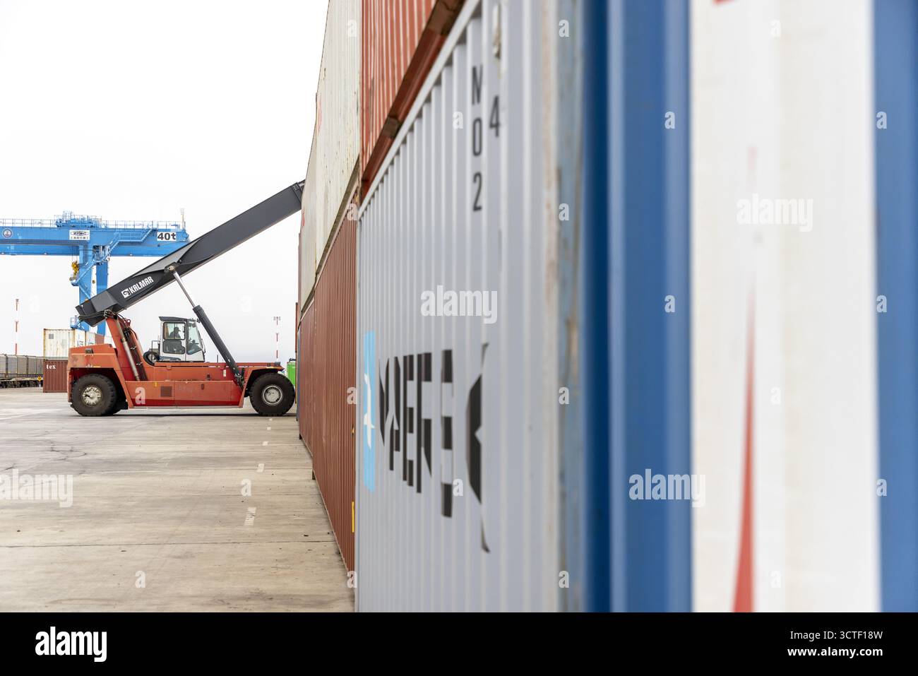 Suswa, Kenia - 07. August 2025: Blick auf einen orangefarbenen Gabelstapler in der Nähe von gestapelten Containern, mit einem blauen Kran in der Ferne. Stockfoto