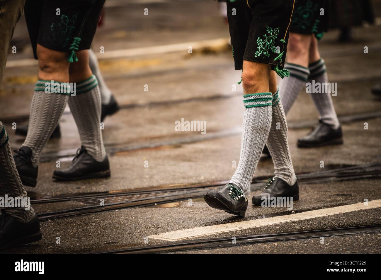 München, Deutschland - 18. September 2022: Blick auf festliche Paradeteilnehmer in traditioneller Kleidung, die geschickt die nasse Straße entlang gehen, ihre gemusterten Socken und polierten Schuhe glänzen. Stockfoto
