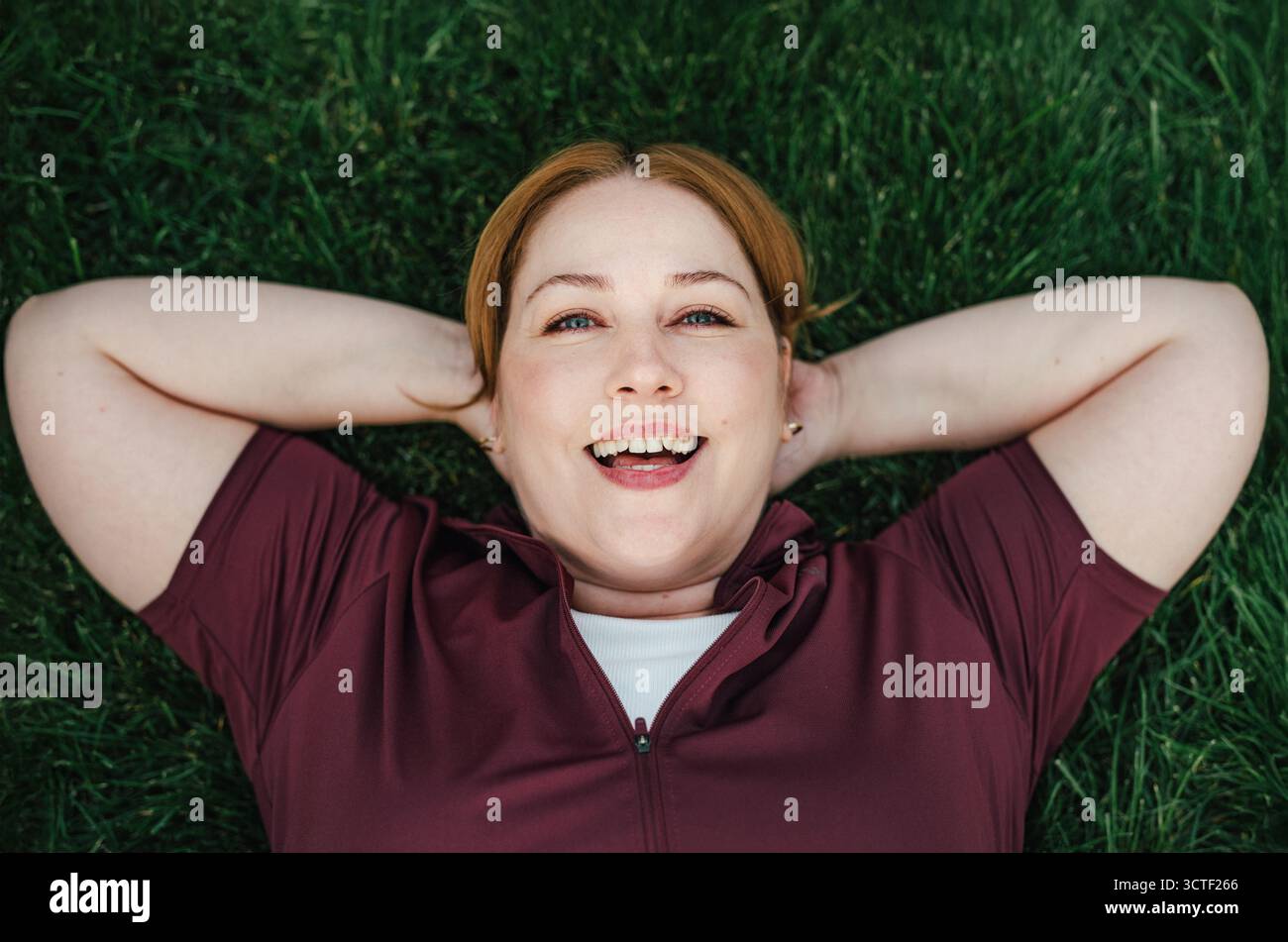 Schöne Frau in Übergröße, die nach dem Training im Freien auf dem Gras liegt. Stockfoto