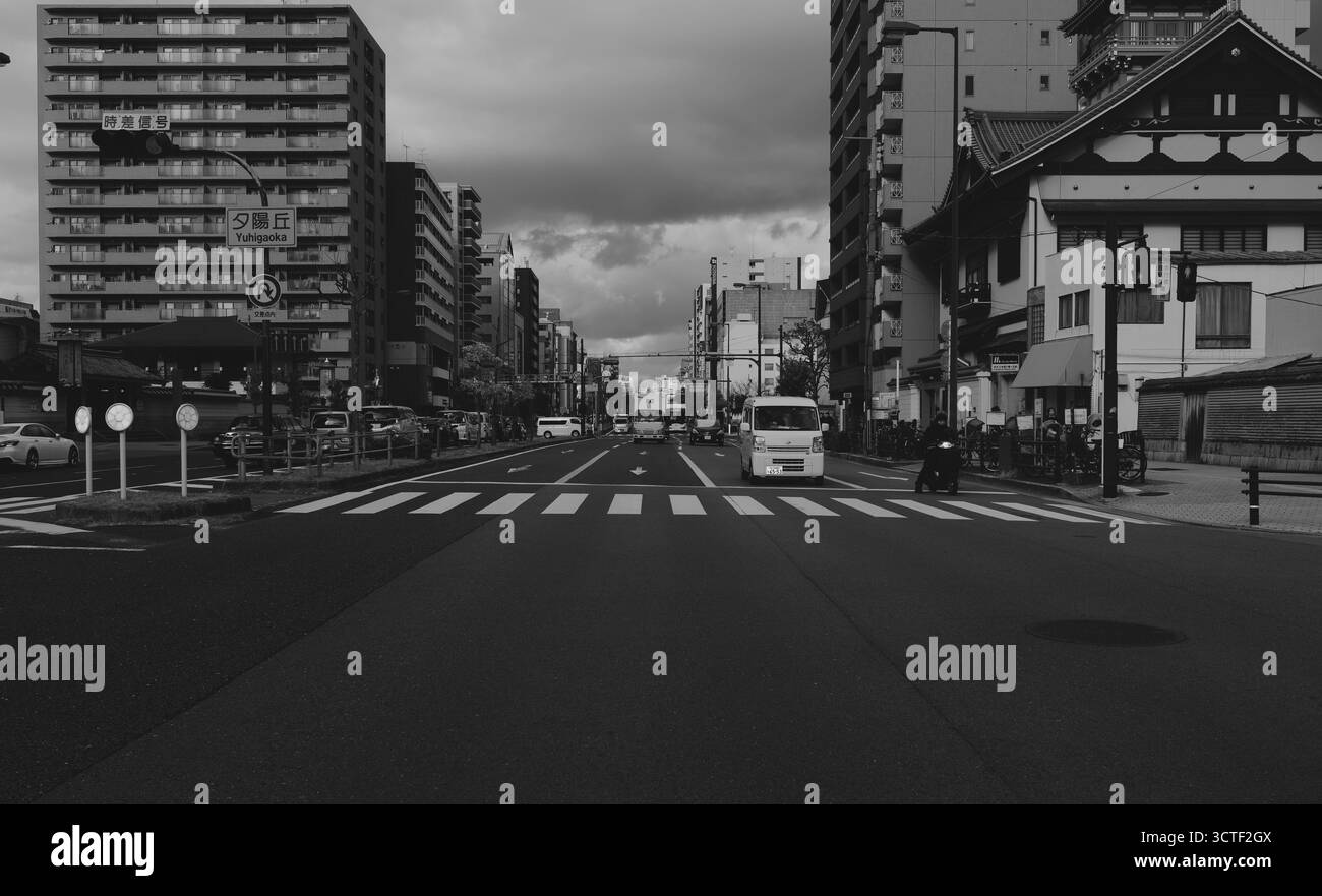 Eine ruhige Straße in Osaka, gesäumt von modernen Apartmentblöcken und traditionellen Gebäuden unter bewölktem Himmel Stockfoto