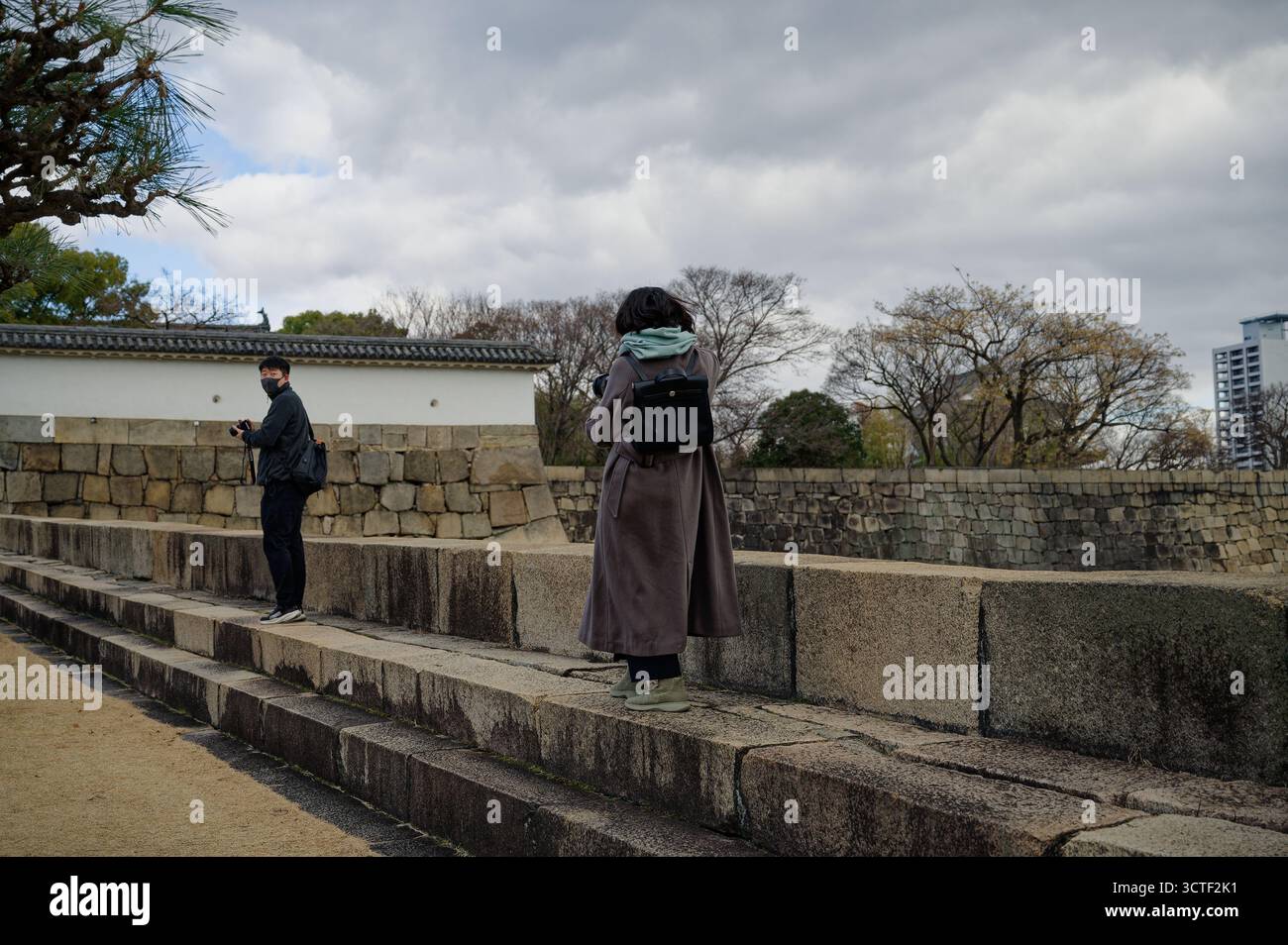 Zwei Besucher erkunden im Winter die Steinmauern von Osaka Castle und machen Fotos zwischen den historischen Befestigungsanlagen Stockfoto
