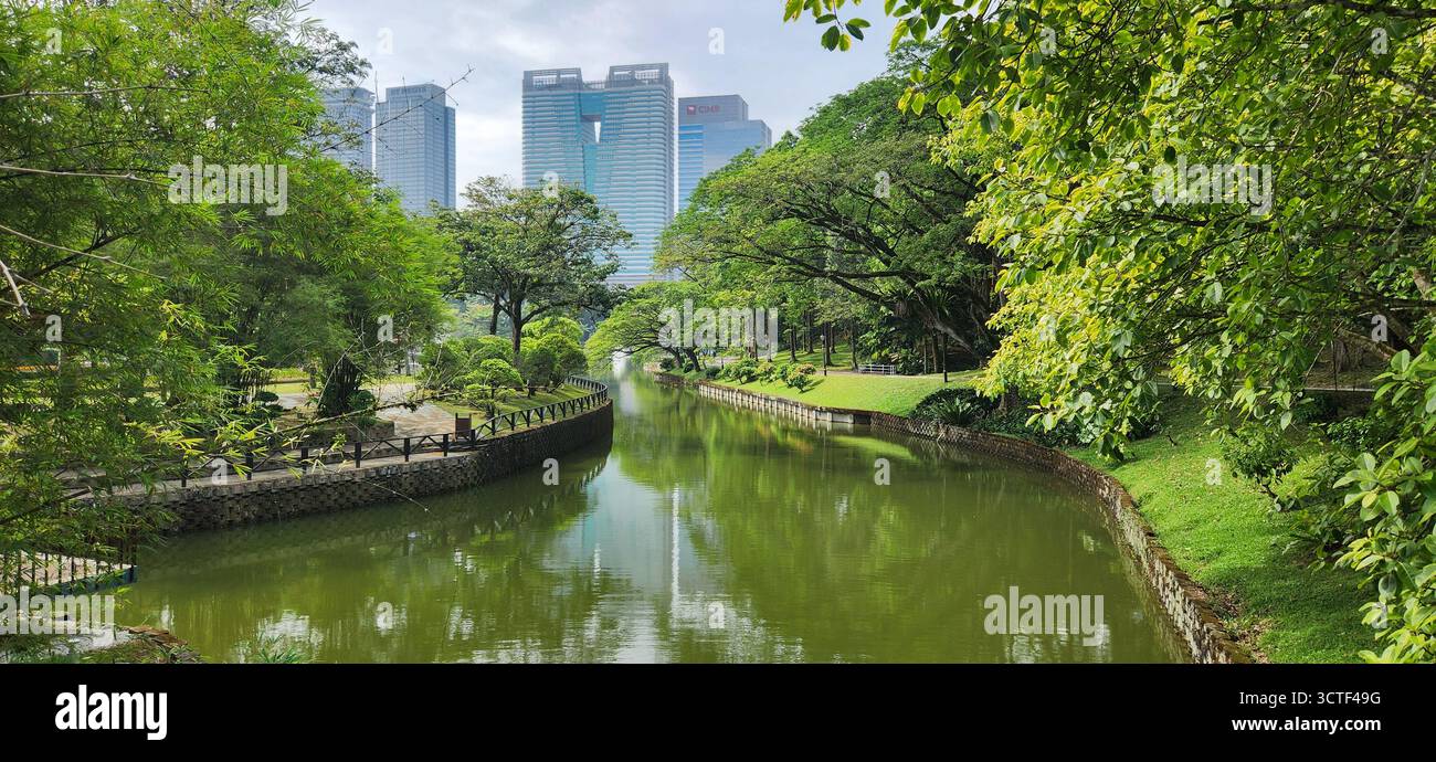 Ein ruhiger Stadtkanal gesäumt von üppigem Grün und modernen Wolkenkratzern im Hintergrund. Stockfoto