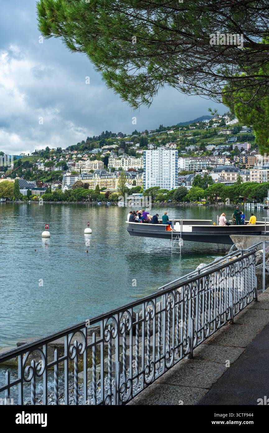 Montreux, Schweiz - 24. September 2025: Malerischer Blick auf eine Seepromenade Montreux mit Menschen, üppigem Grün und Gebäuden auf einem Hügel. Stockfoto