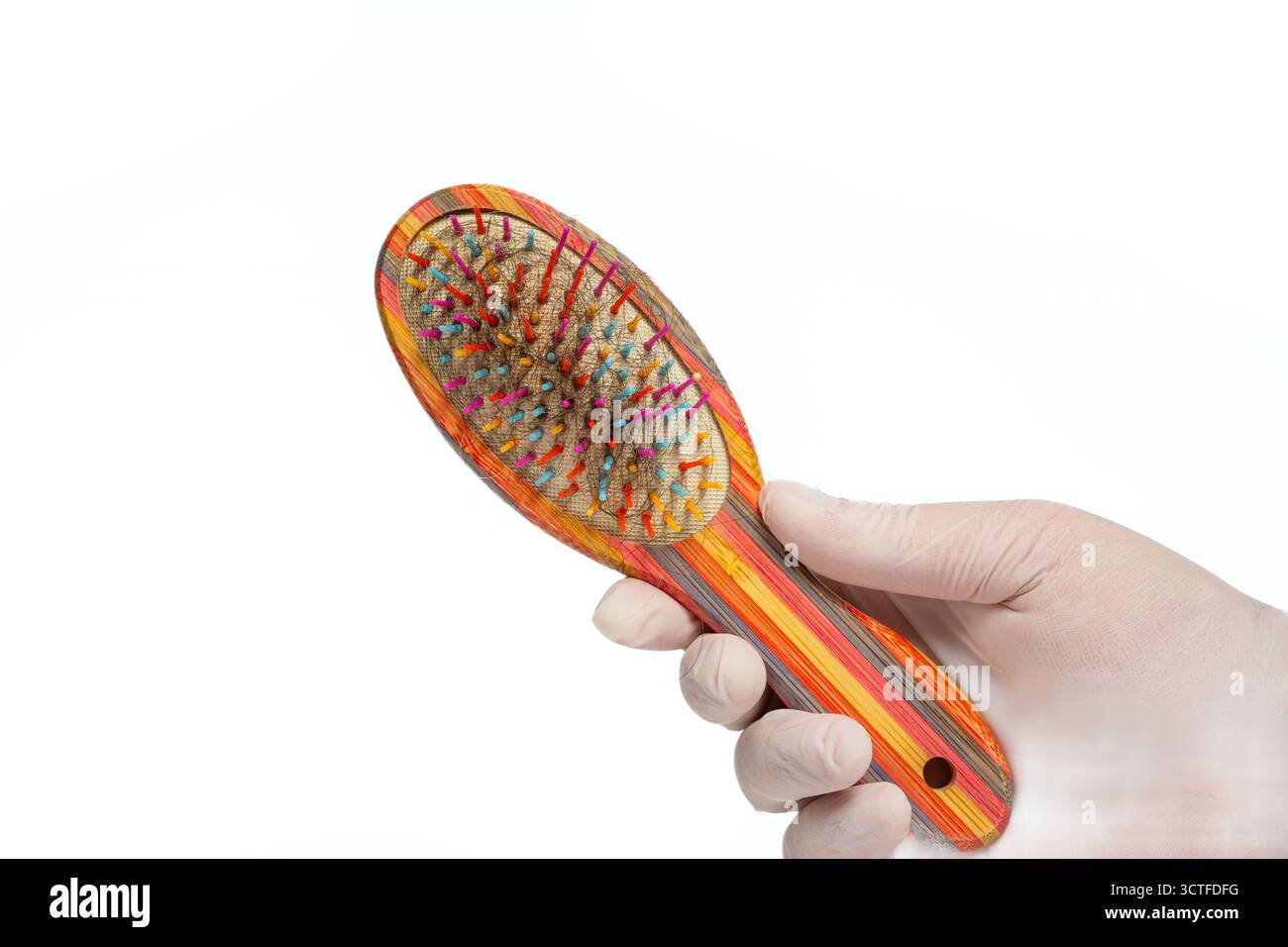 Hand mit Handschuhen, die bunte Haarbürste mit losen Haarsträhnen in Borsten auf isoliertem weißem Hintergrund hält. Pflege, Pflegeprobleme Stockfoto