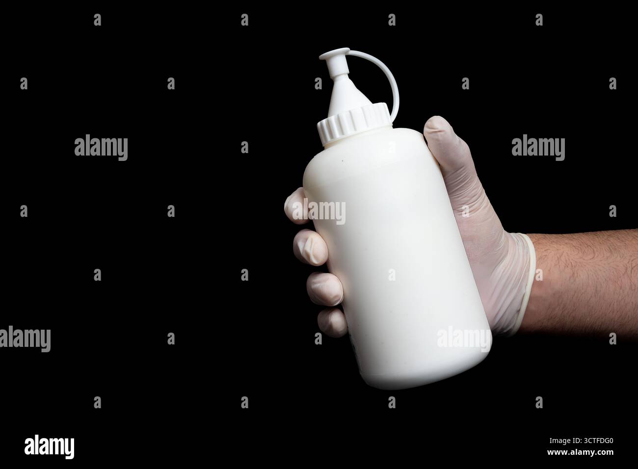 Hand in Latexhandschuhen, die eine weiße Plastikflasche mit Düsenkappe auf isoliertem schwarzen Hintergrund halten. Nachfüllbarer Kunststoffspender für Flüssigkeiten und Stockfoto