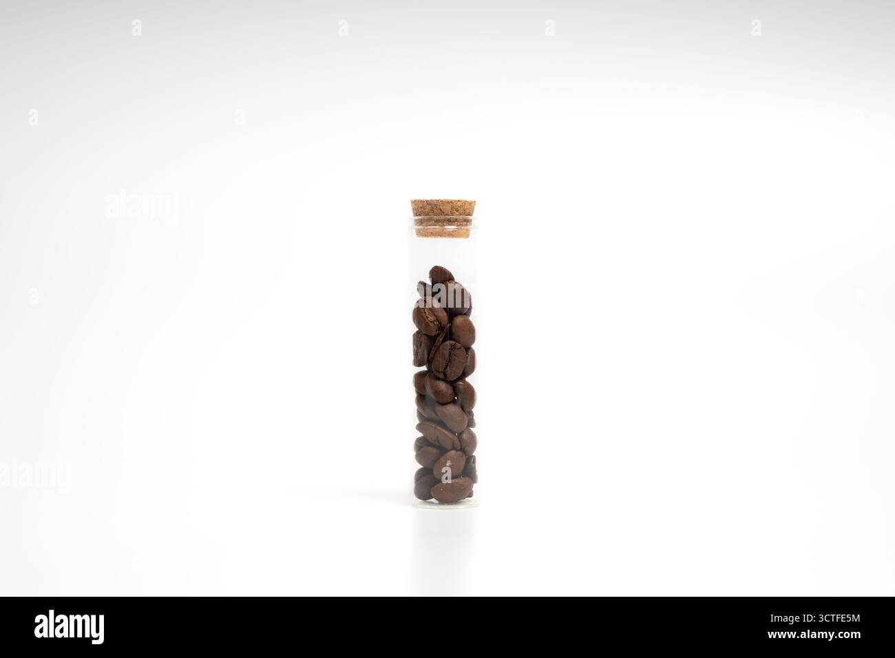 Glasröhre mit Korkdeckel gefüllt mit braunen Kaffeebohnen auf isoliertem weißem Hintergrund. Kaffeezubereitung, Aroma, Brüh- und Lagerkonzept Stockfoto