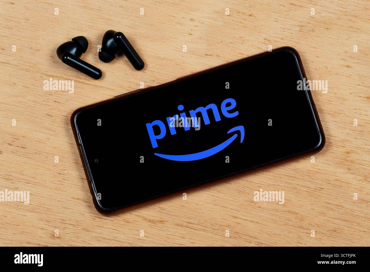 Nahaufnahme eines schnurlosen Ohrhörers mit einem Smartphone mit blauem amazon Prime Video-Logo auf hölzernem Hintergrund Stockfoto