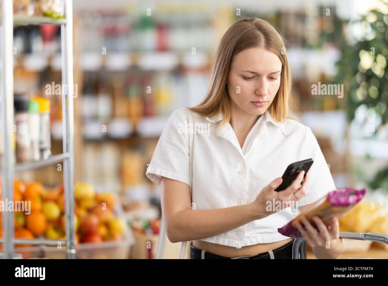 Prüfen des Ablaufdatums von Spaghetti – weibliche Käuferinnen scannen den QR-Code auf dem Etikett von Spaghetti mit Smartphone Stockfoto