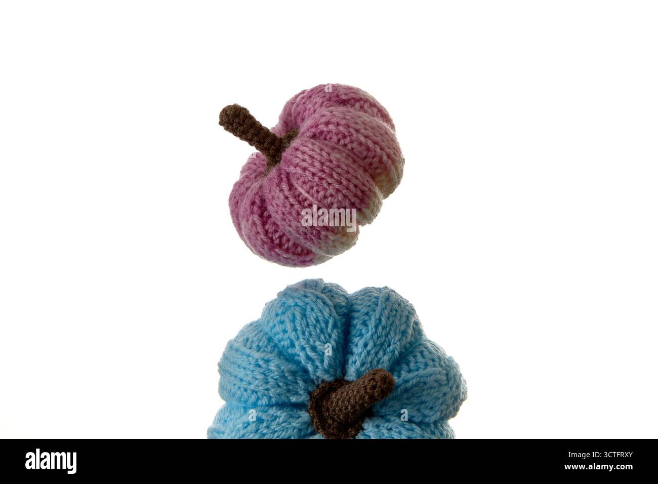 Bunte blaue und rosa handgefertigte Strickkürbisse auf weißem Hintergrund. Herbstliches und gemütliches Wohnkultur-Konzept ideal für Bastelarbeiten, Heimwerkerprojekte und Stockfoto