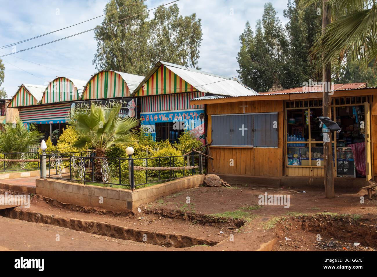 Fenote Selam, Äthiopien – 20. April 2019: Lokale Unternehmen mit amharischen Schildern und einem kleinen umzäunten Garten arbeiten nebeneinander im Stadtzentrum. Stockfoto