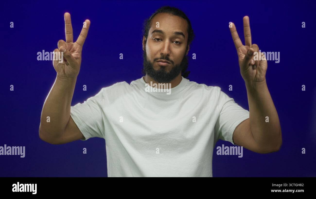 Mann, der mit Händen im Studio vor tiefblauem Hintergrund Luftzitierungen zeigt, mit weißem T-Shirt und Bart; Sarkasmus-Ironie. Stockfoto