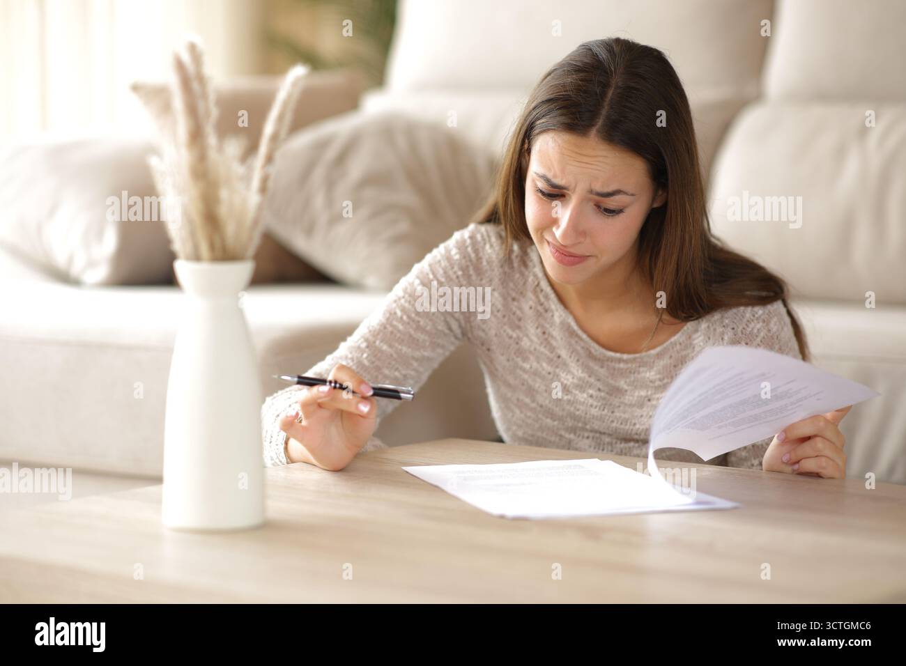 Verwirrte Frau liest Vertrag, um zu Hause auf einem Couchtisch zu unterschreiben Stockfoto