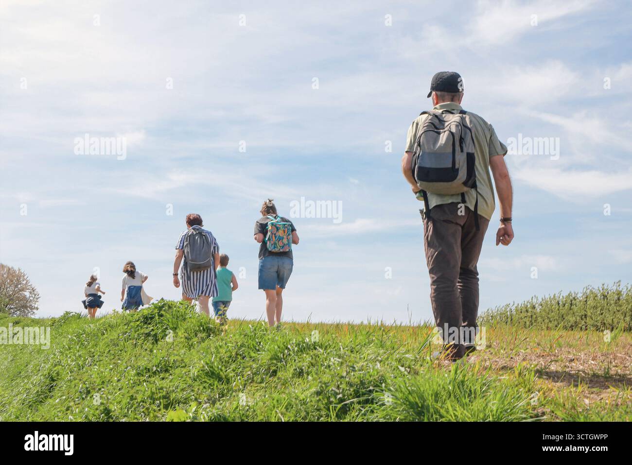 Eine Gruppe von Menschen läuft auf einem grasbewachsenen Hügel. Einer der Leute trägt einen Rucksack Stockfoto