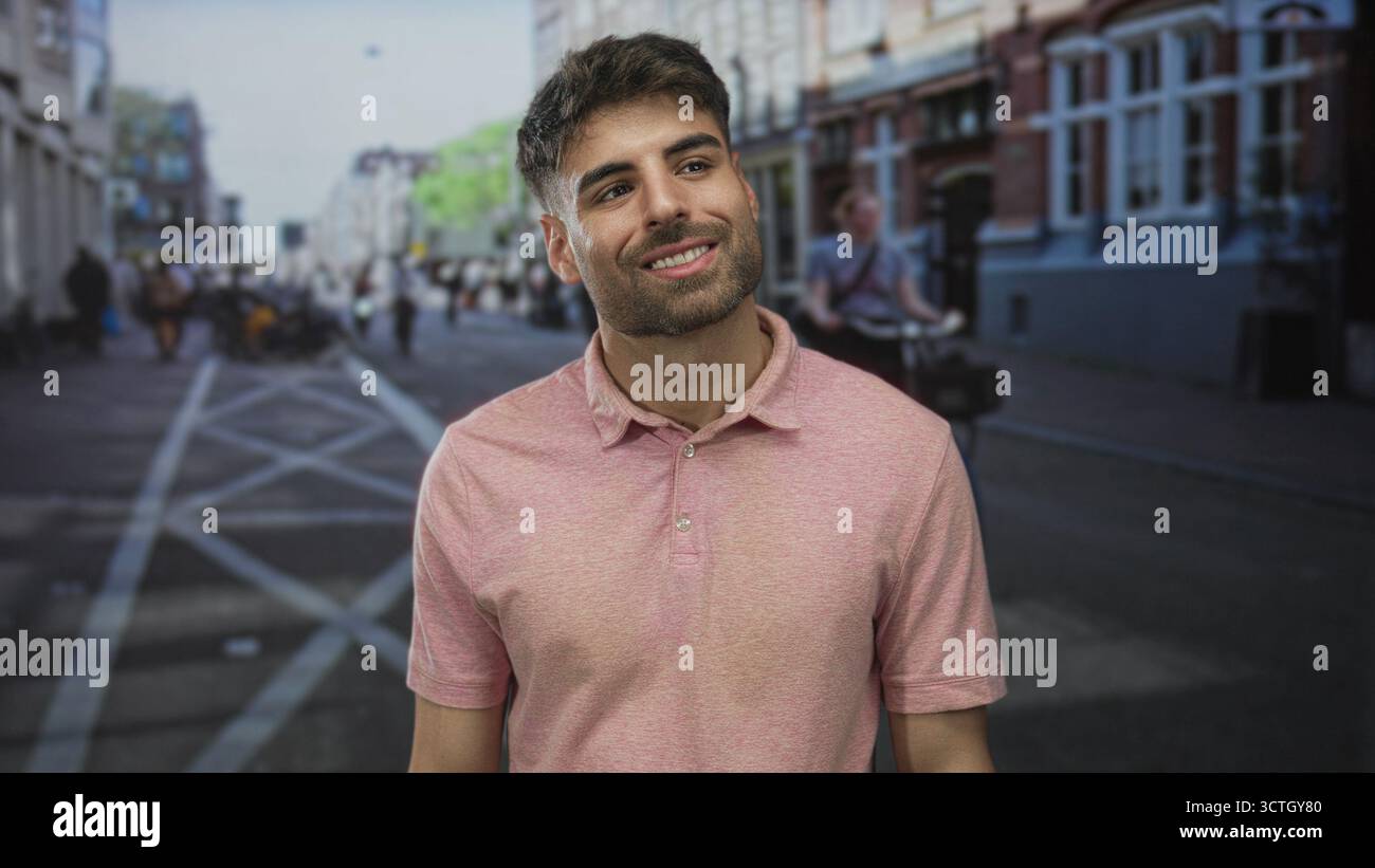 Mann lächelt in einem rosa Polo auf einer überfüllten Stadtstraße mit verschwommenen Fußgängern und Gebäuden im Blick; Glück. Stockfoto
