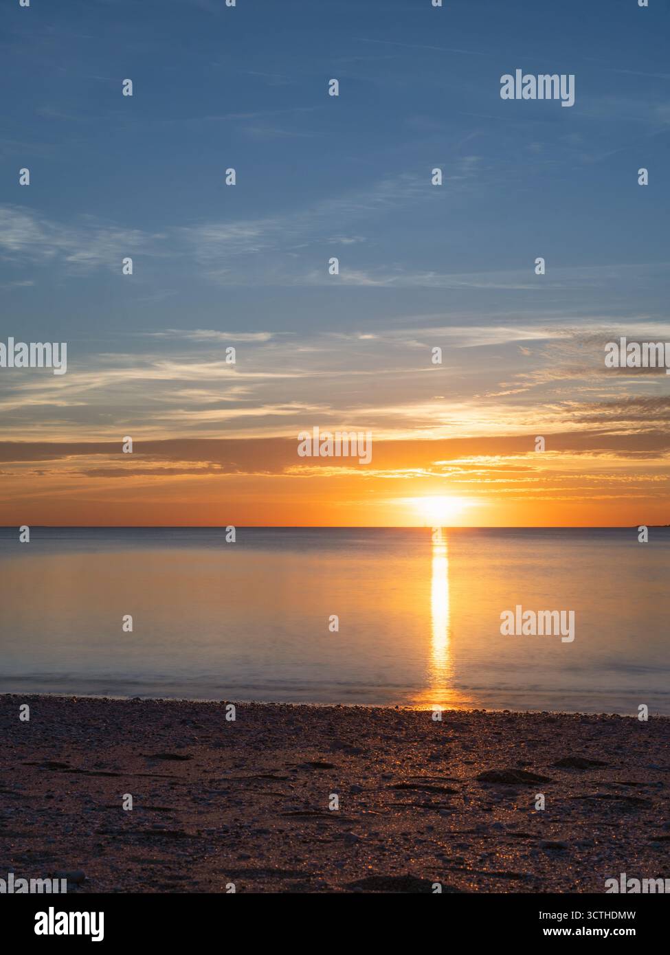 Der friedliche Sonnenuntergang beleuchtet den Meereshorizont und schafft eine perfekte goldene Reflexion auf dem stillen Wasser Stockfoto
