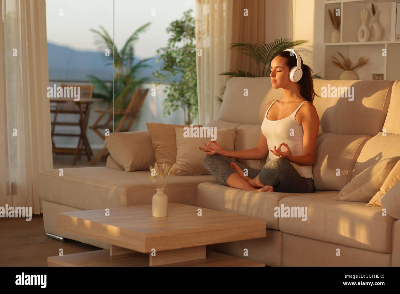 Yogi hören Yoga-Kurs von Kopfhörern, die zu Hause auf einer Couch sitzen Stockfoto