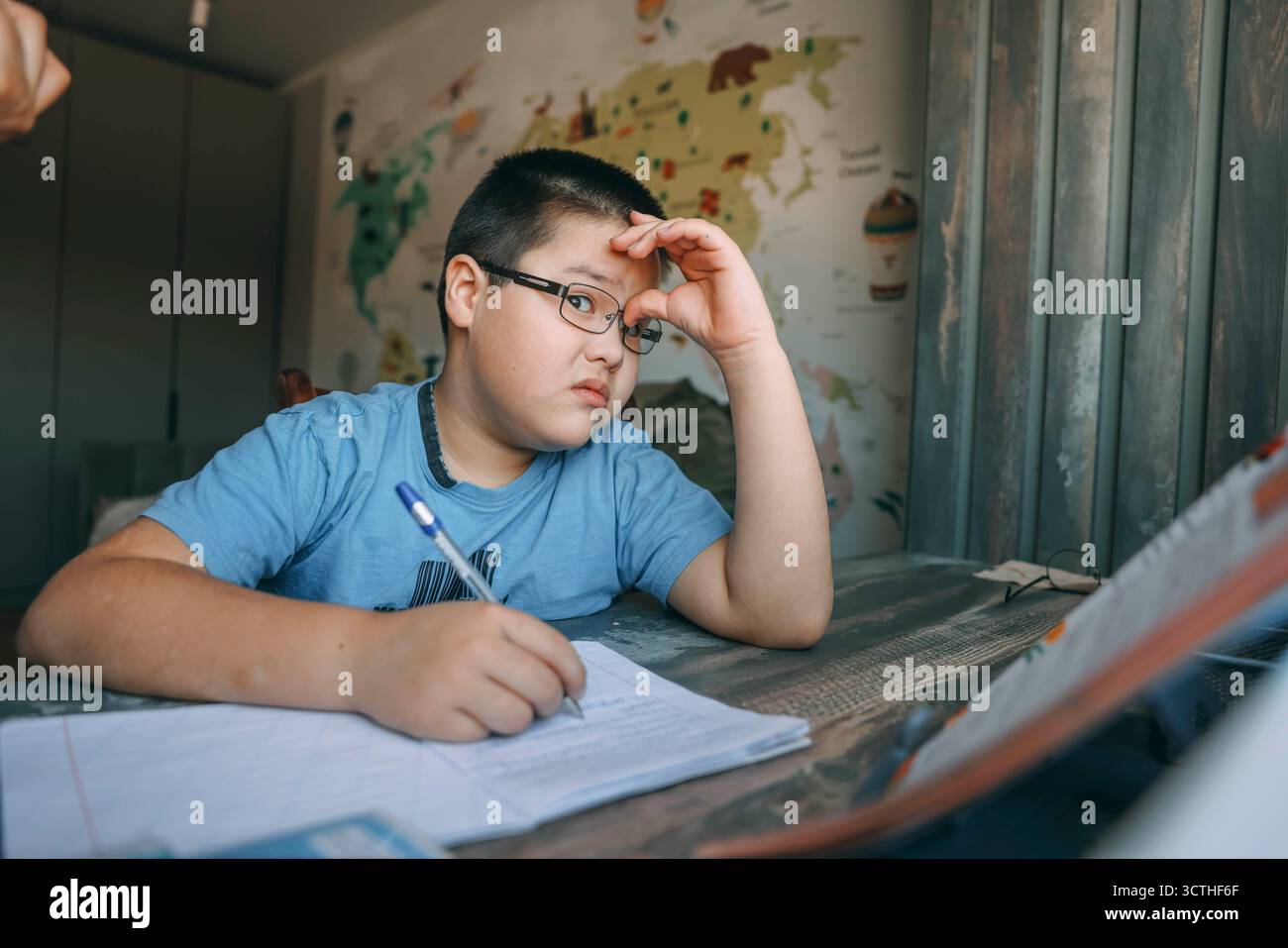 Asiatischer Junge mit einer Brille, die frustriert den Kopf hält, Schulaufgabe am Schreibtisch in der Nähe der Welt, Landkarte, Konzept der Hausschulung, Bildungsdienst Stockfoto