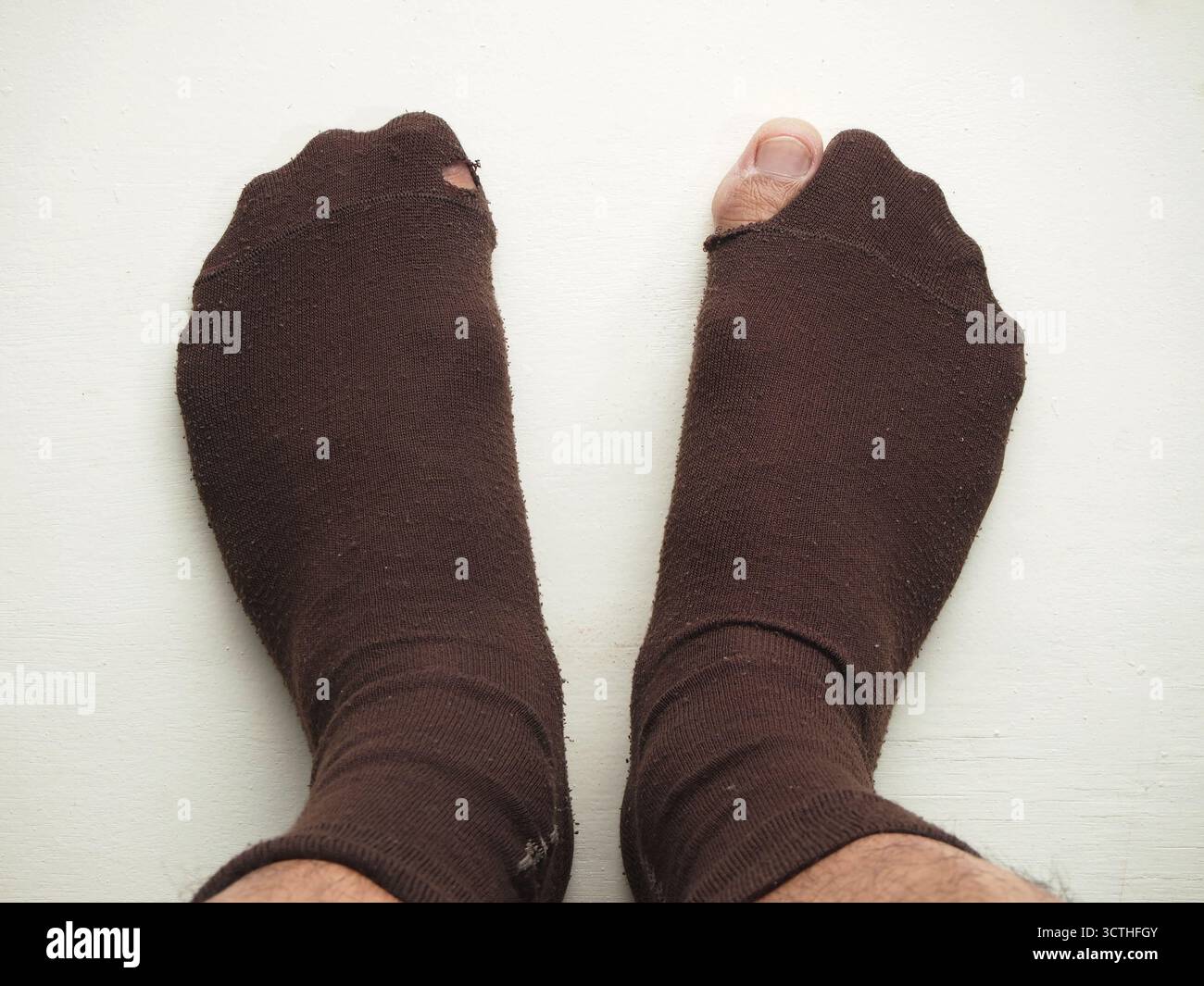 Eine Draufsicht auf ein Paar Füße, die braune Socken mit kleinen und großen Löchern tragen, sodass die große Zehe des rechten Fußes herausragt Stockfoto