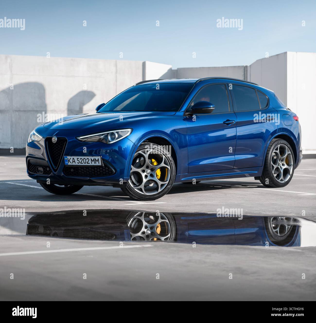 Blaues Alfa Romeo vor dem modernen Gebäude. Vorderansicht des sportlichen italienischen SUV in urbaner Umgebung, reflektiert in der Pfütze am Boden. Stockfoto