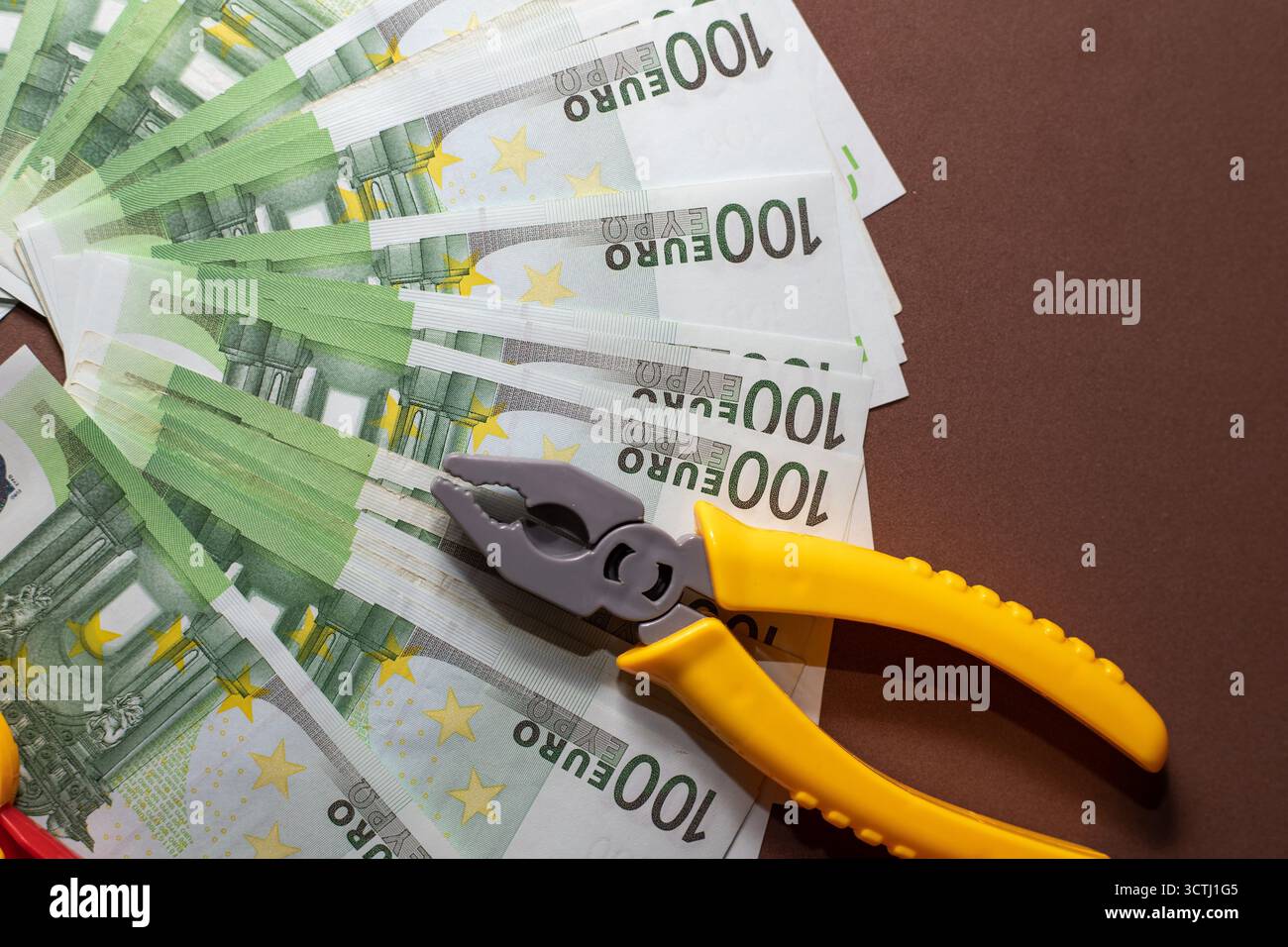 Gelbe Spielzeugzange auf einem Fächer von 100-Euro-Banknoten auf braunem Hintergrund. Konzept der Finanzkontrolle, Geschäftsstrategie und Geldmanagement. Stockfoto