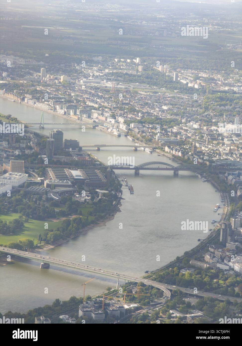 Aus der Vogelperspektive sehen Sie den sich windenden Rhein mit Brücken und die Kölner Skyline. Üppiges Grün umgibt das Wasser, unter hellem Himmel während der Dayli Stockfoto