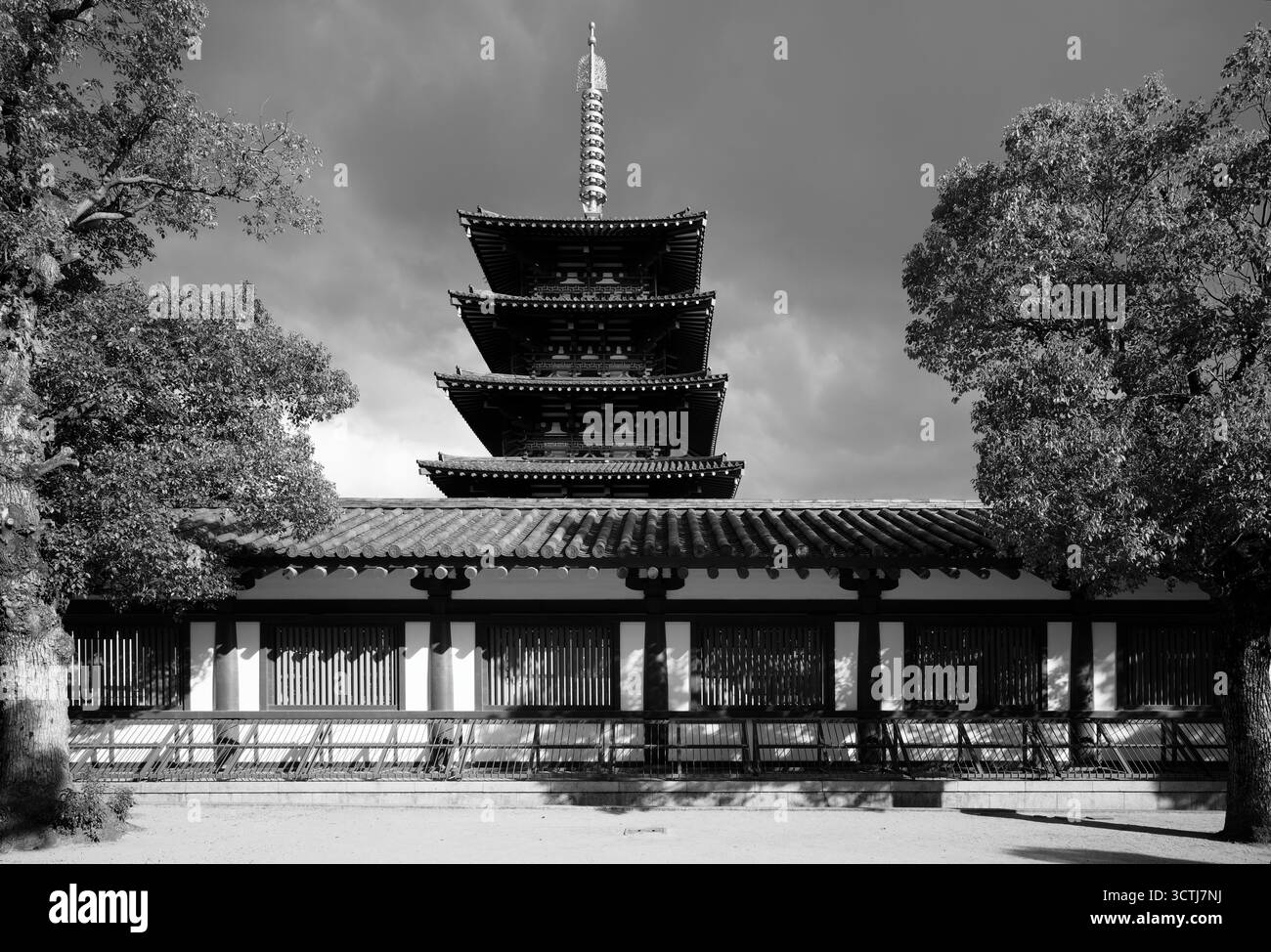 Die Pagode erhebt sich hinter den Tempelmauern in Osaka, eingerahmt von hohen Bäumen unter einem dramatischen Himmel in Schwarz-weiß Stockfoto