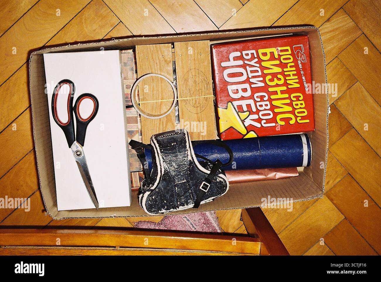 Ein Umzugskarton gefüllt mit Scheren, einer alten Kamera und Büchern während eines Hausumzugs, fotografiert mit direktem Analogblitz und nostalgischen Filmtonwerten. Stockfoto