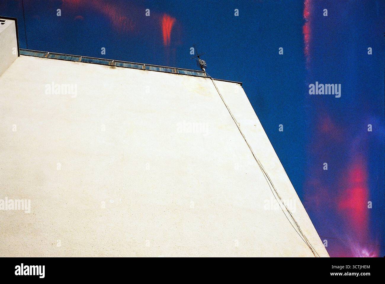 Seite eines fensterlosen Wohngebäudes, das von der Wintersonne beleuchtet wird; ein TV-Antennenkabel und rotes Licht, das von einem Olympus Mju austritt, schaffen eine minimale Szene. Stockfoto