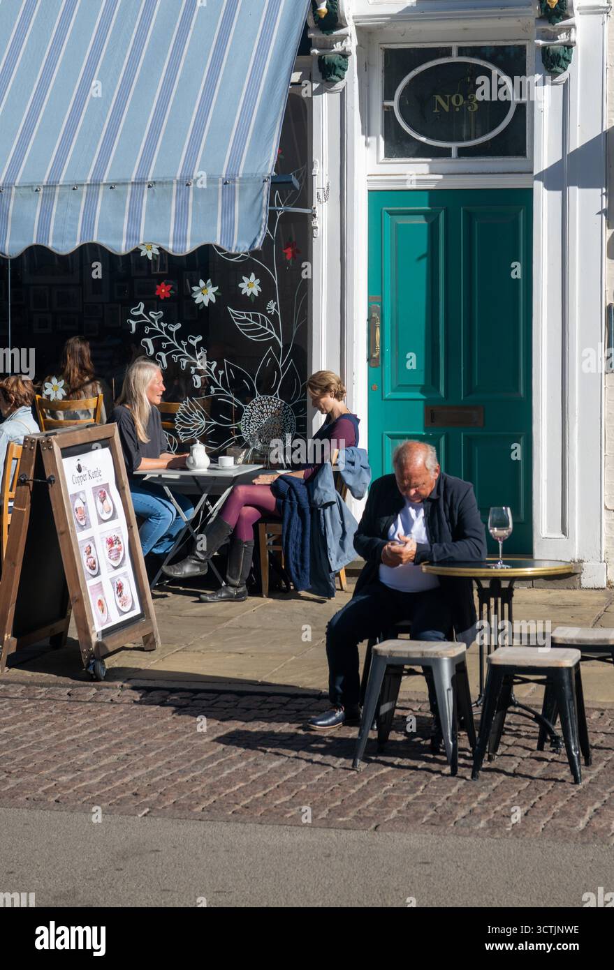Menschen, die vor einem Café auf der King’s Parade in Cambridge sitzen und einen sonnigen Tag in der historischen Universität genießen Stockfoto