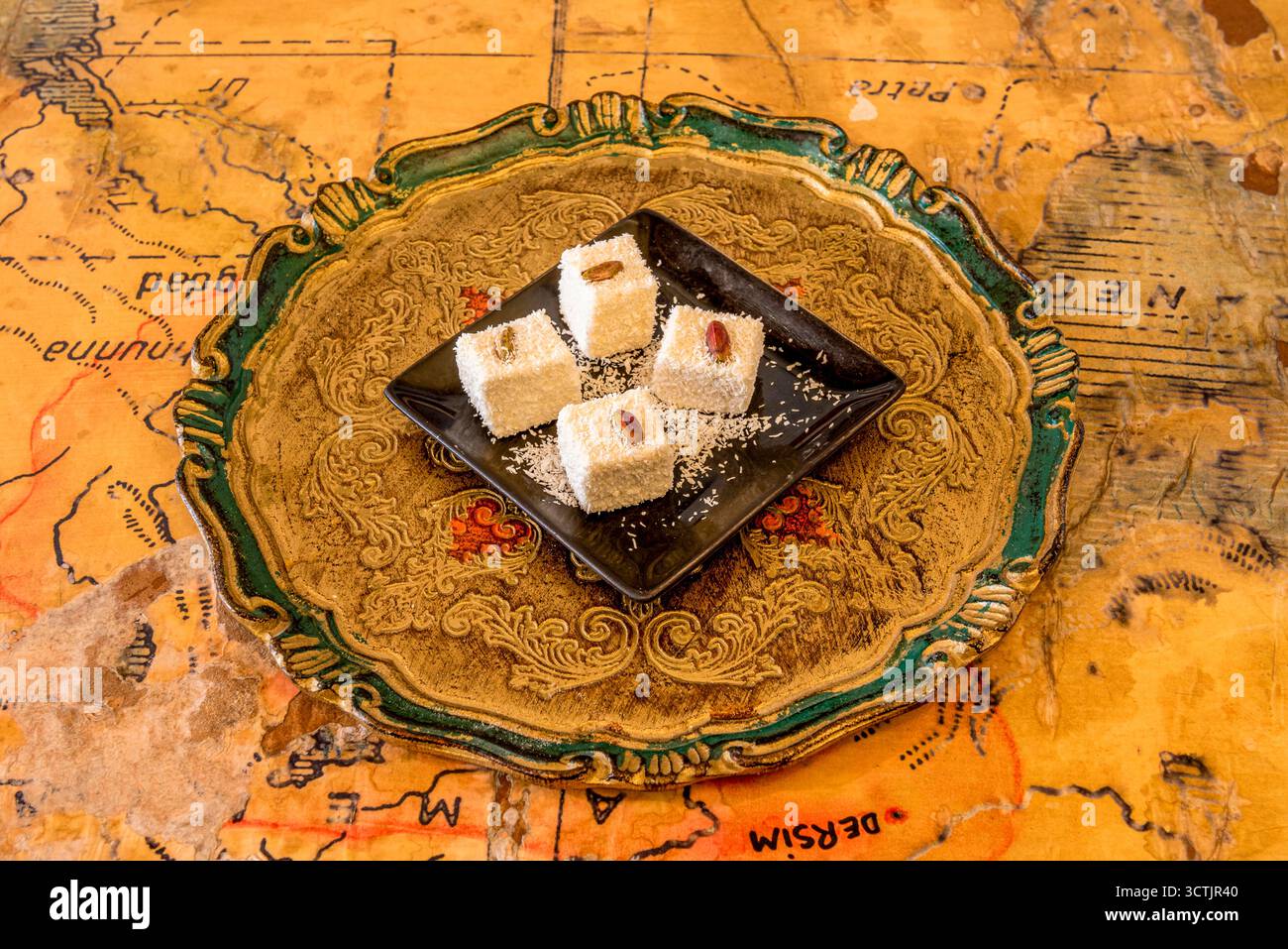 Vier Stücke türkischer Delight mit Pistazie auf der Oberseite und mit Kokosnuss-Kratzer auf schwarzem Teller bestreut Stockfoto