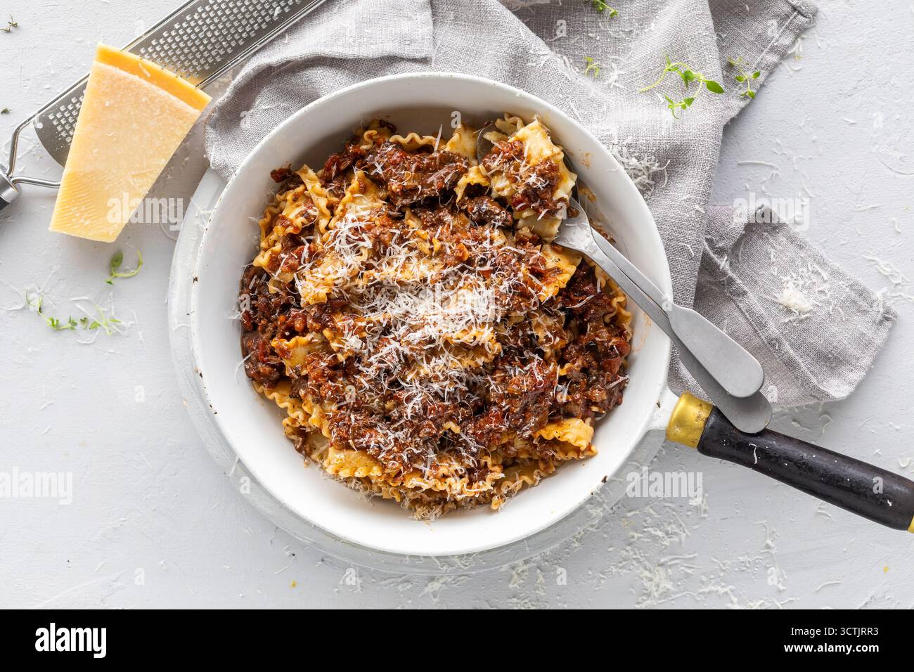 Hausgemachtes Rindfleischragu auf Pasta mit geriebenem Parmesan, fotografiert bei weichem Tageslicht auf strukturiertem weißem Hintergrund für italienische Komfortgerichte. Stockfoto