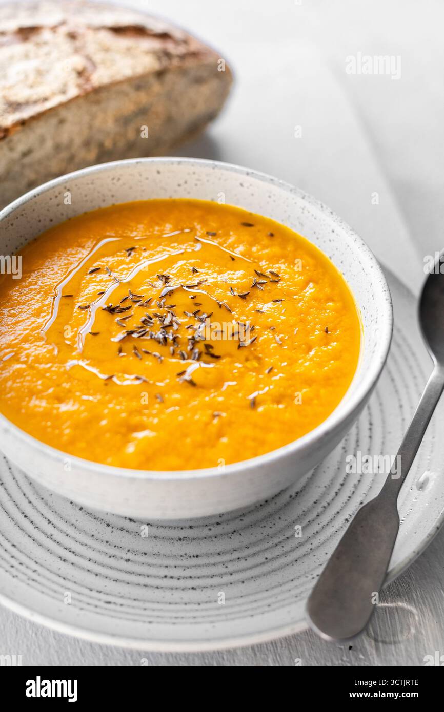 Helle Karotten- und Zitronengras-Suppe mit Kümmel und Olivenöl, serviert mit rustikalem Brot bei natürlichem Tageslicht. Stockfoto