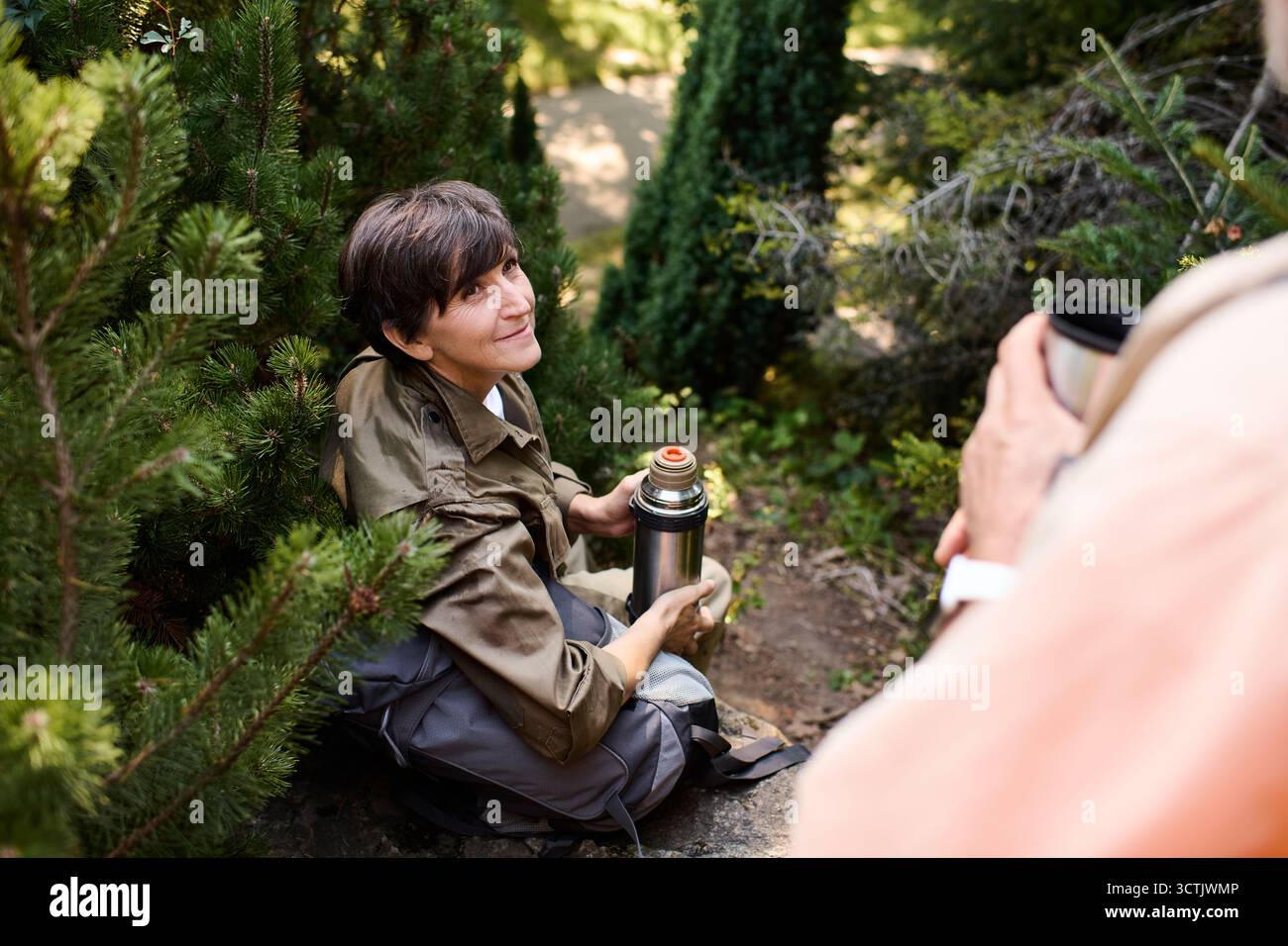 Aktive Senioren wandern durch üppiges Grün, teilen Momente und warme Getränke auf einem Bergpfad. Stockfoto
